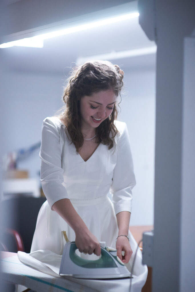 A bride irons the skirt of the wedding dress she is wearing.